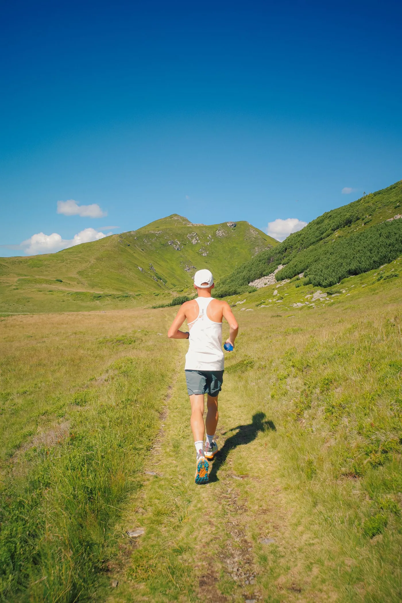 Un coureur de dos sur un sentier de montagne, entre des prairies, un matin d'été